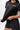 Flow Women's Tech Tee in black, upper-body view of a model pulling the hem out to show the stretch, white Gracie Barra Stacked logo on the left chest