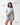 Flow Women's Tech Tee in light grey, full-length view of a model pulling the hem out to show the stretch, dark Gracie Barra Stacked logo on the left chest