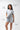 Flow Women's Tech Tee in light grey, full-length view of a model pulling the hem out to show the stretch, dark Gracie Barra Stacked logo on the left chest
