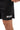 Frame Men's Short in black, close-up of a hand pulling the hem out to show the side hem vent, white Gracie Barra Stacked logo on the lower left leg