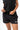 Frame Women's Short in black, front view with both hands adjusting the drawstring waistband, white Gracie Barra Stacked logo on the lower left leg