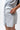 Frame Women's Short in light grey, close-up of a hand opening the zippered back pocket and side hem vent, white Gracie Barra Stacked logo partly in frame