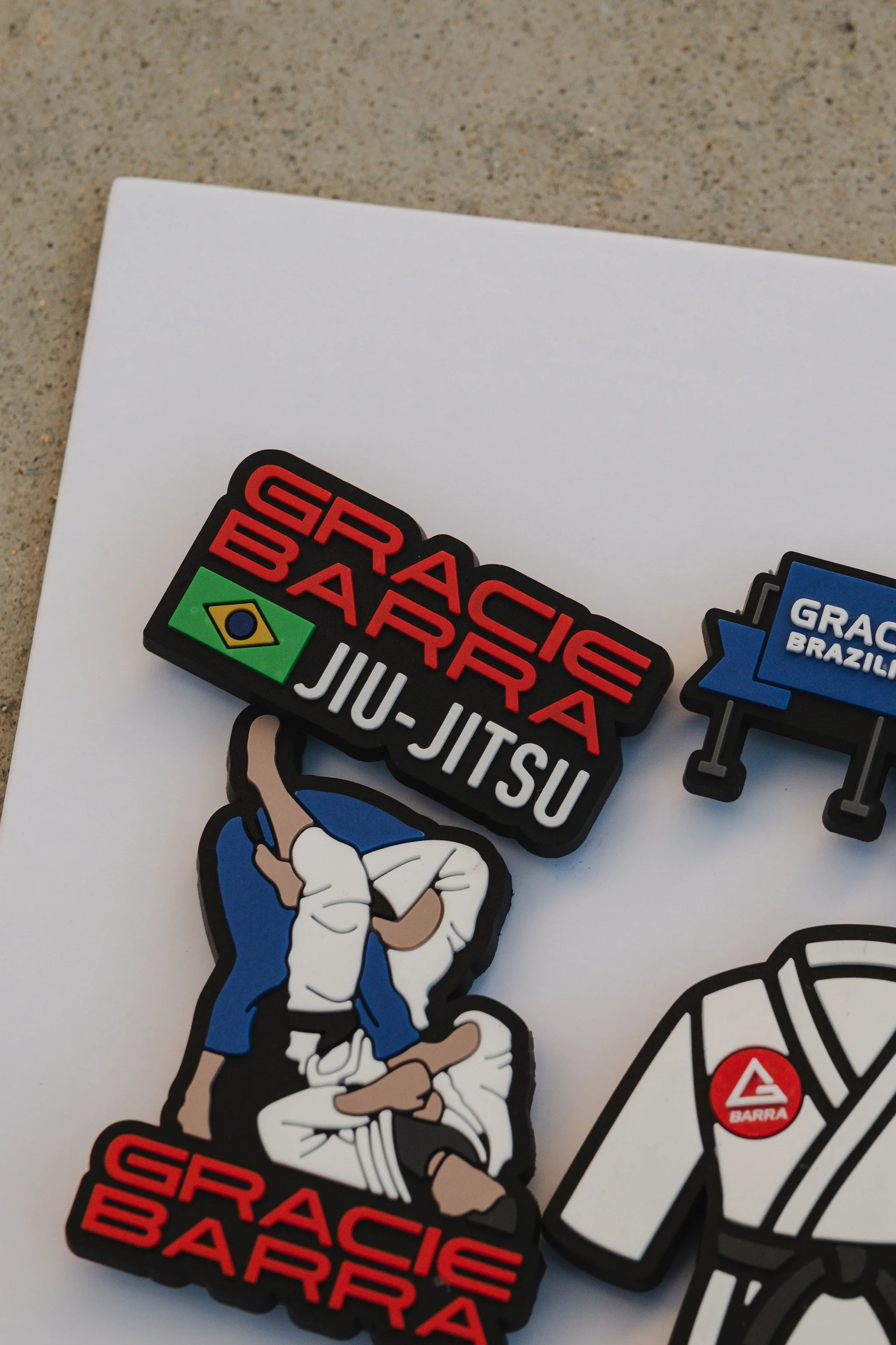 Macro view of the GB Jiu-Jitsu logo charm and grappling illustration charm positioned on the white display card.