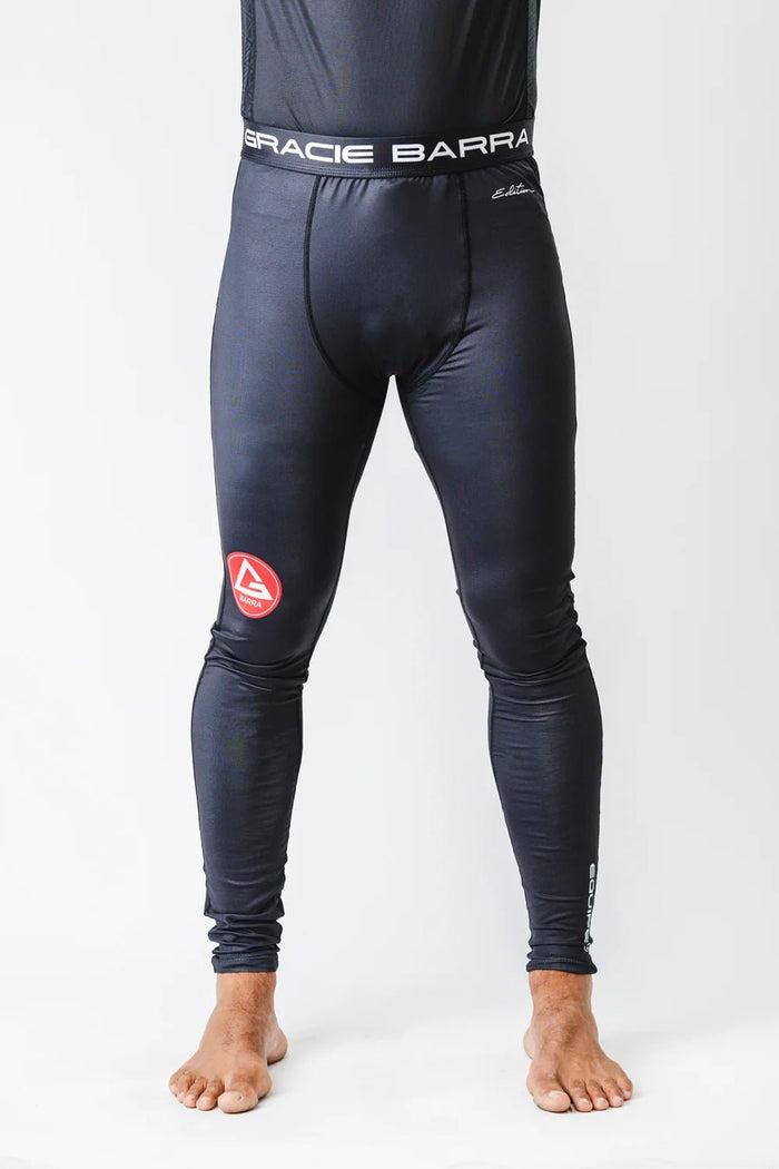 Model wearing black GB Essentials compression pants, front view showing Gracie Barra waistband and red logo on the left thigh
