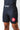 Angled front view of a man in black GB Essentials velcroless training shorts showing the Gracie Barra waistband logo, red triangle leg patch and side leg split