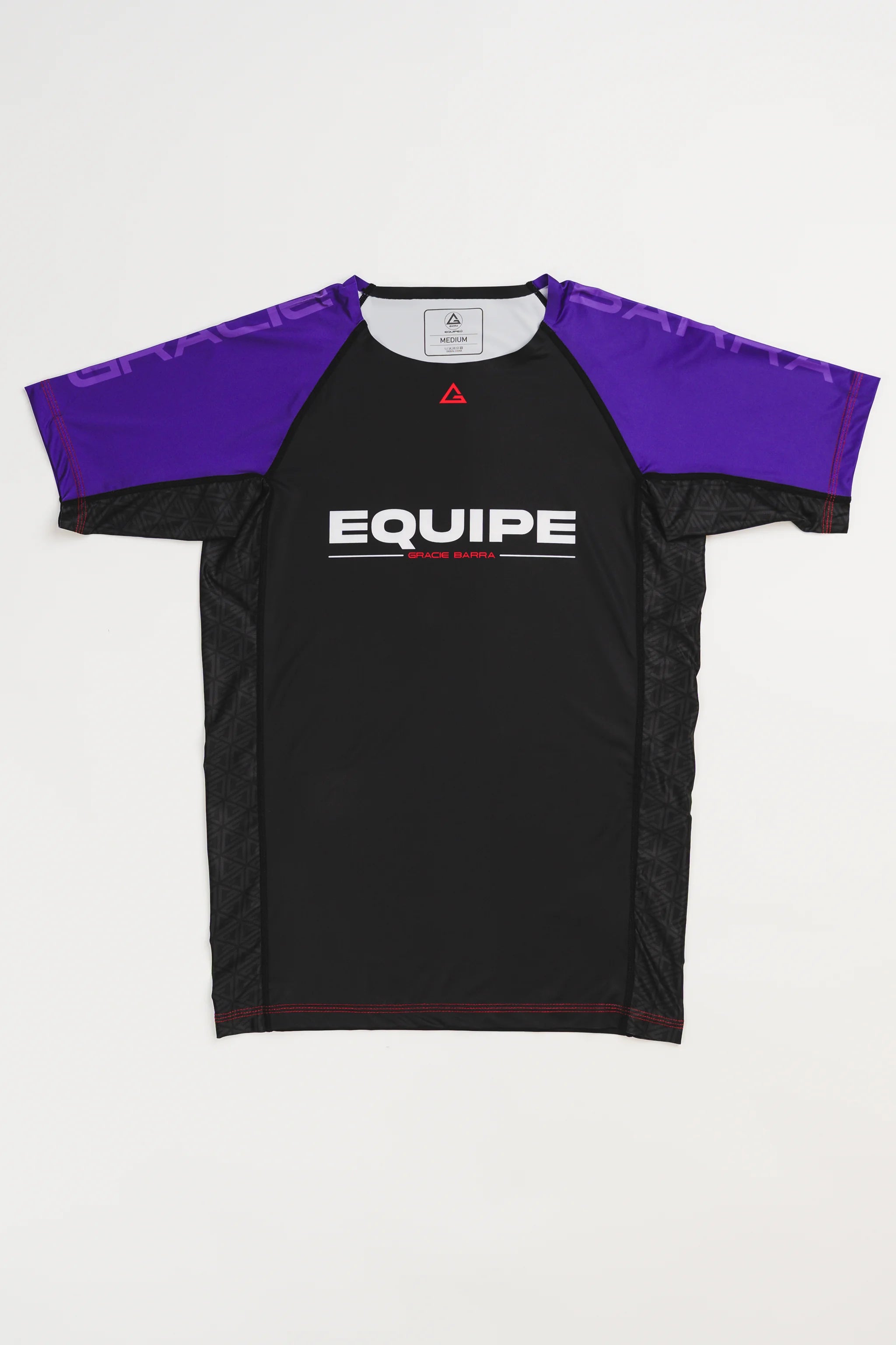 GB Essentials Women’s Rashguard in purple colorway, front layflat view with black body, purple sleeves, and EQUIPE Gracie Barra wordmark across the chest, finished with red stitching details.