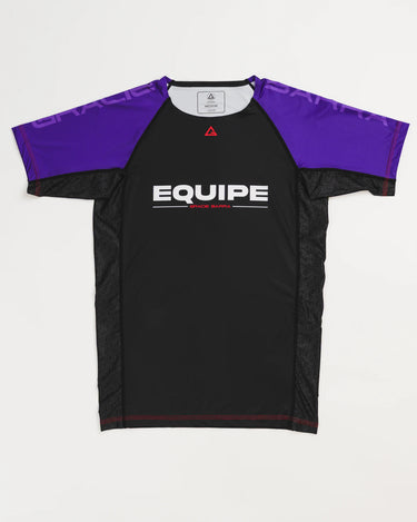 GB Essentials Women’s Rashguard in purple colorway, front layflat view with black body, purple sleeves, and EQUIPE Gracie Barra wordmark across the chest, finished with red stitching details.