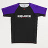 GB Essentials Women’s Rashguard in purple colorway, front layflat view with black body, purple sleeves, and EQUIPE Gracie Barra wordmark across the chest, finished with red stitching details.