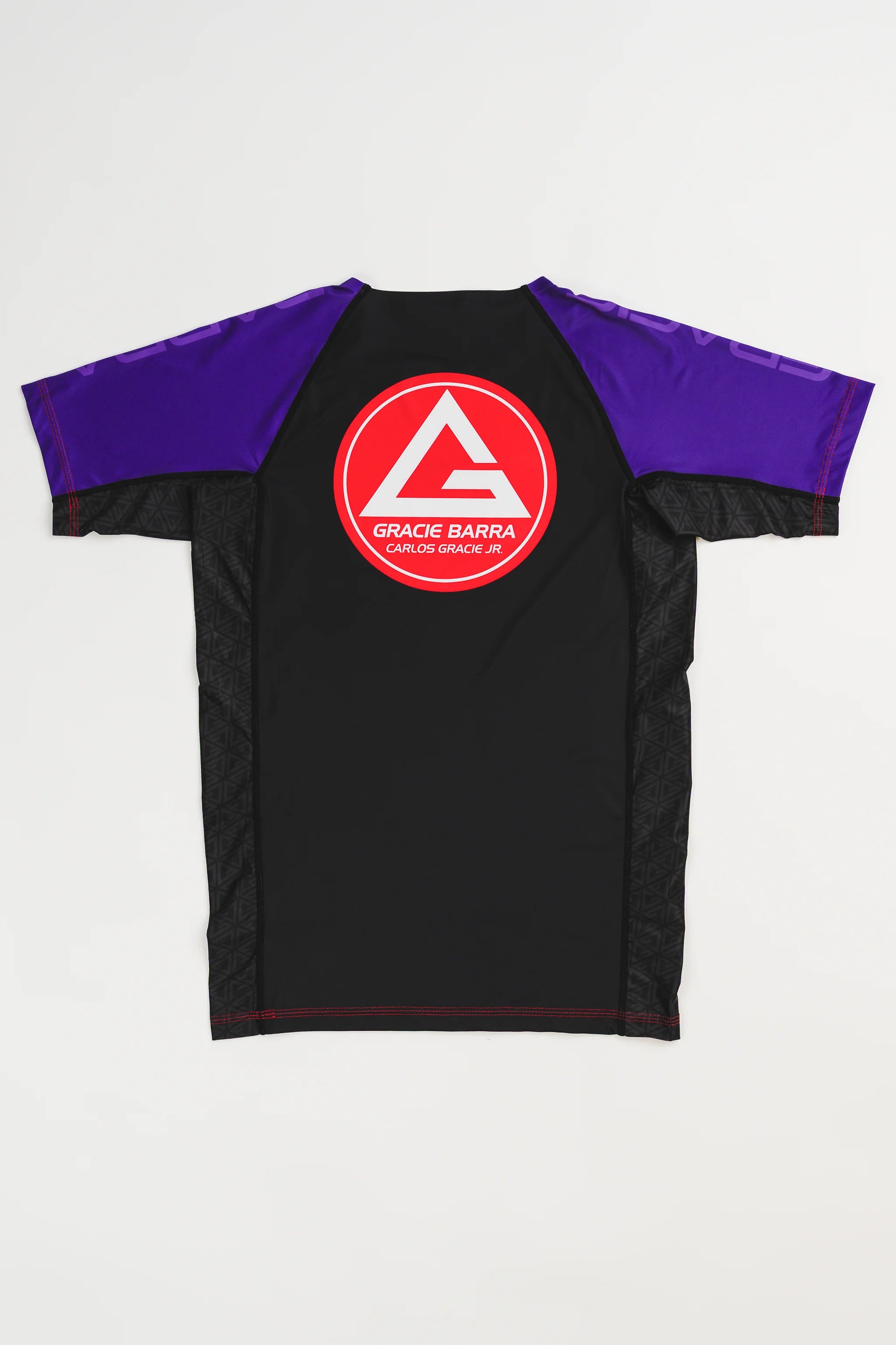 Back view of GB Essentials Women’s Rashguard in purple colorway, featuring the Gracie Barra Red Shield logo centered on the back with contrast stitching and geometric side panels.
