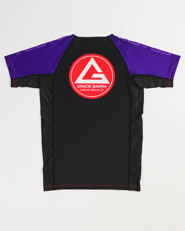 Back view of GB Essentials Women’s Rashguard in purple colorway, featuring the Gracie Barra Red Shield logo centered on the back with contrast stitching and geometric side panels.
