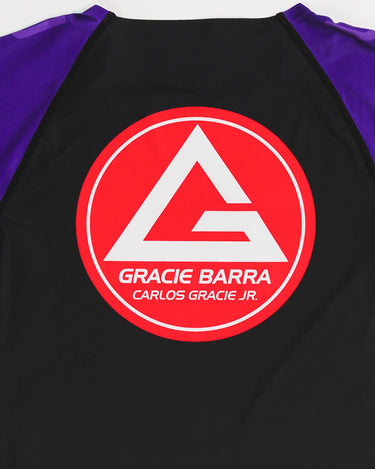 Close-up of the Gracie Barra Red Shield logo with Carlos Gracie Jr. signature on the back of the GB Essentials Women’s Rashguard in purple colorway.