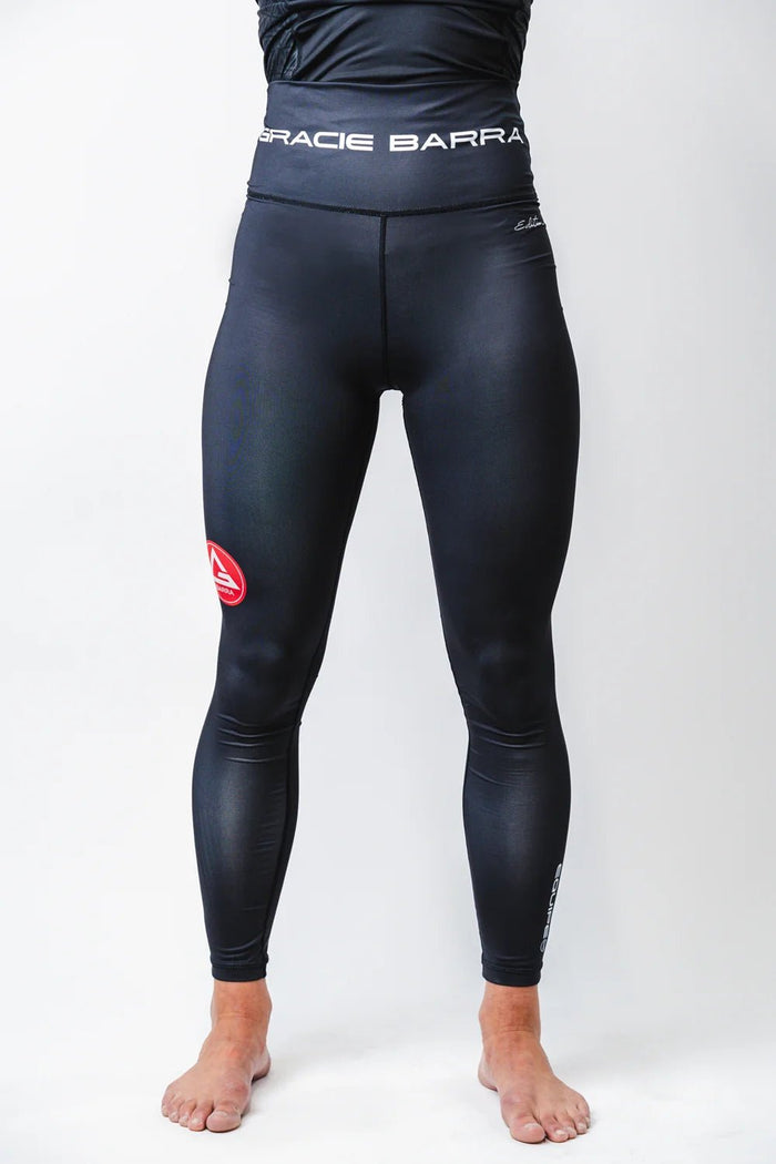 Front view of the black GB Essentials Womens Compression Pants showing the high waistband, tapered full-length fit, and red Barra Shield patch.