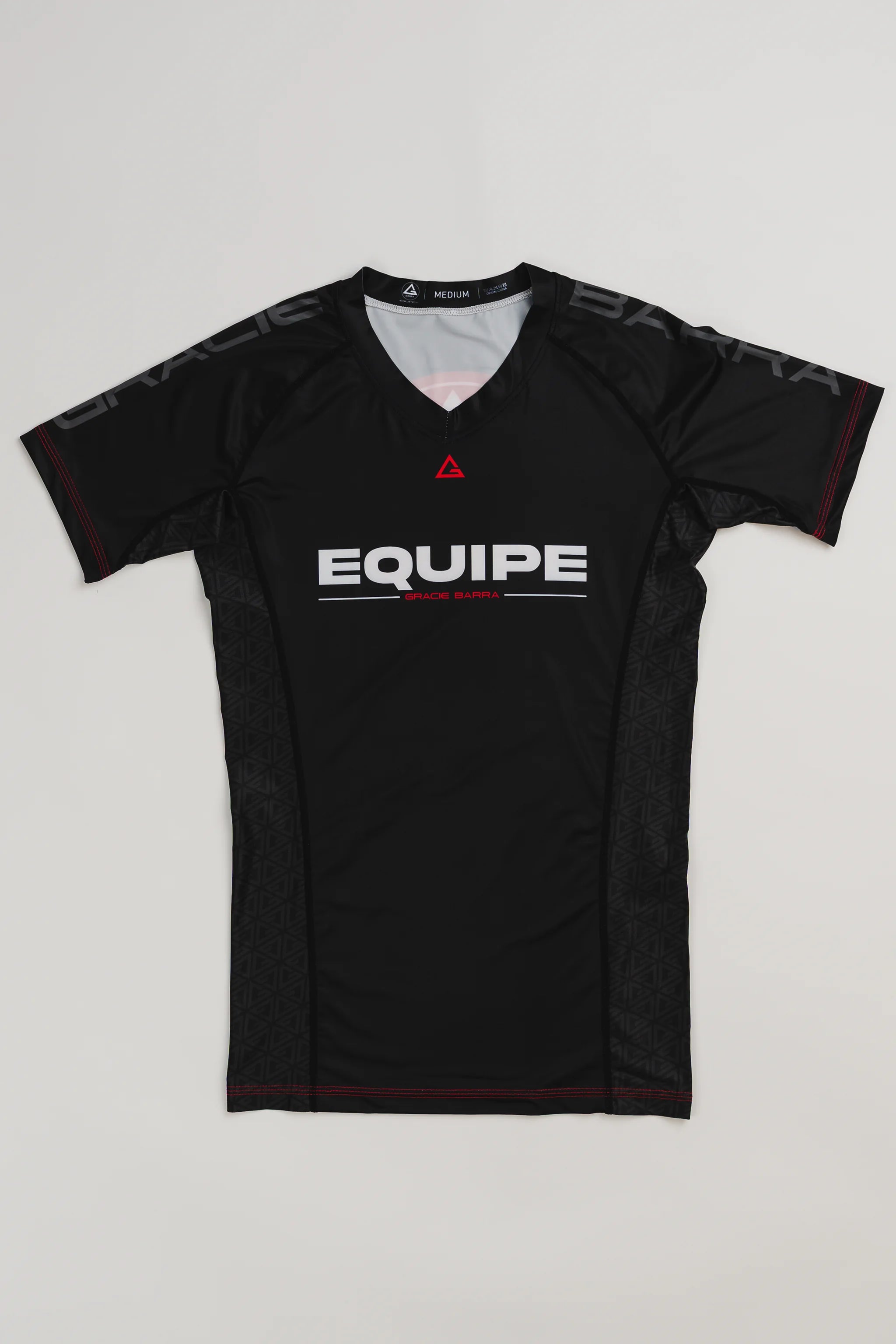 GB Essentials Women’s Ranked Rashguard in black with short sleeves, Gracie Barra Equipe branding, and red stitching accents, laid flat on a white background.