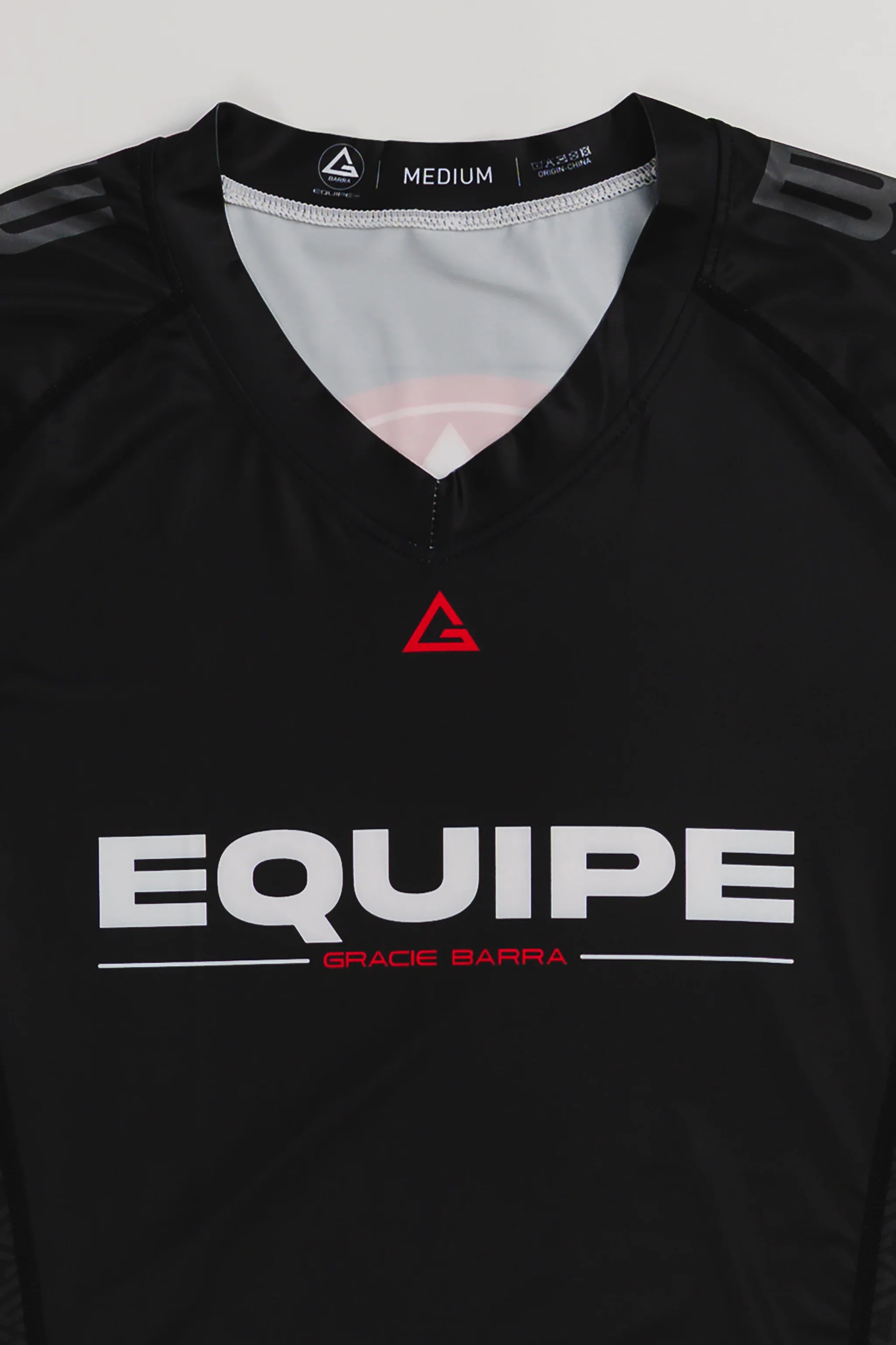 Close-up of GB Essentials Women’s Ranked Rashguard in black, showing Legacy G logo and sweat-wicking stretch fabric.