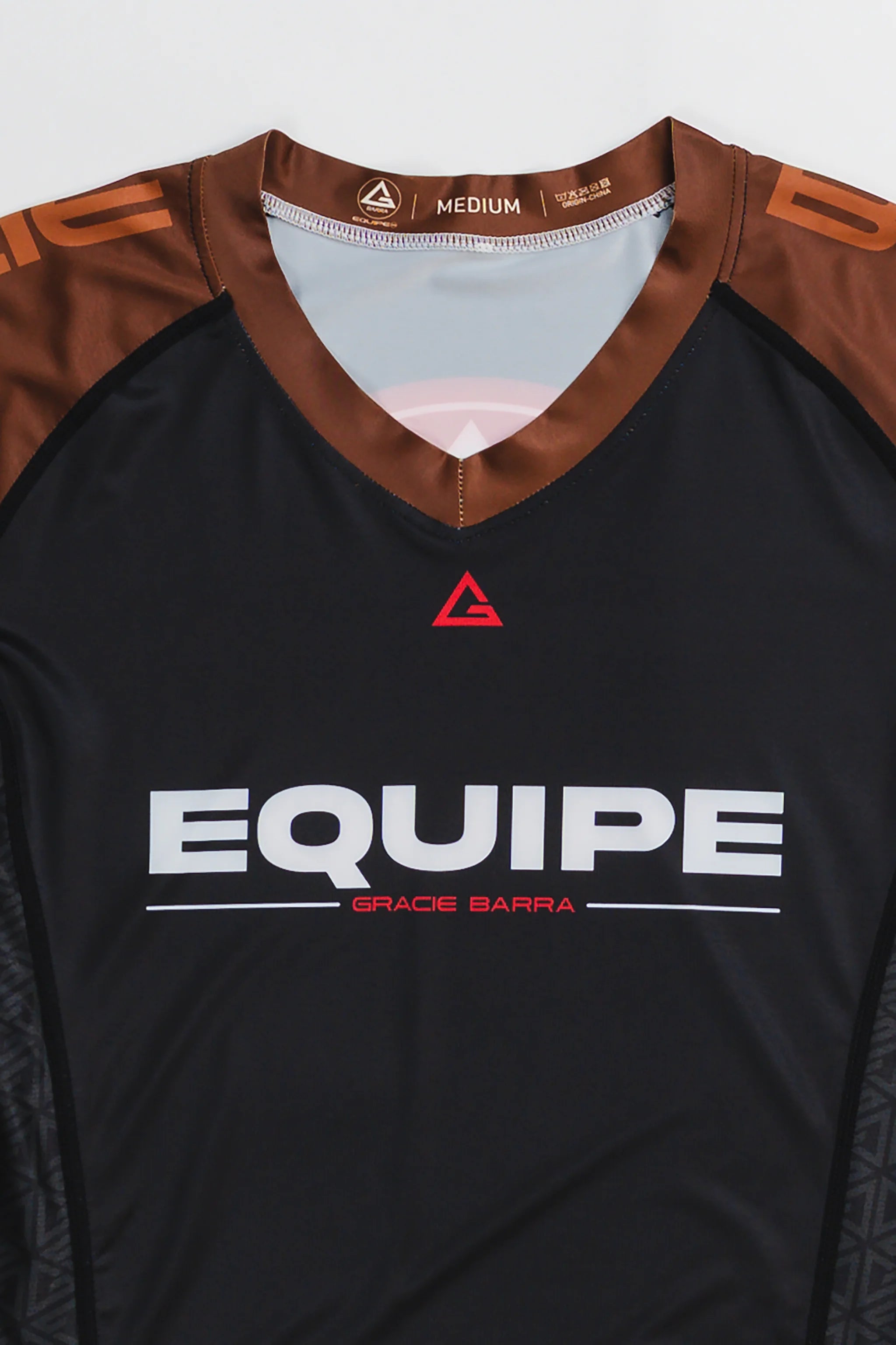 GB Essentials Women’s Ranked Rashguard in black with brown shoulders, featuring the Equipe Gracie Barra wordmark across the chest and red Legacy G logo at the collar.