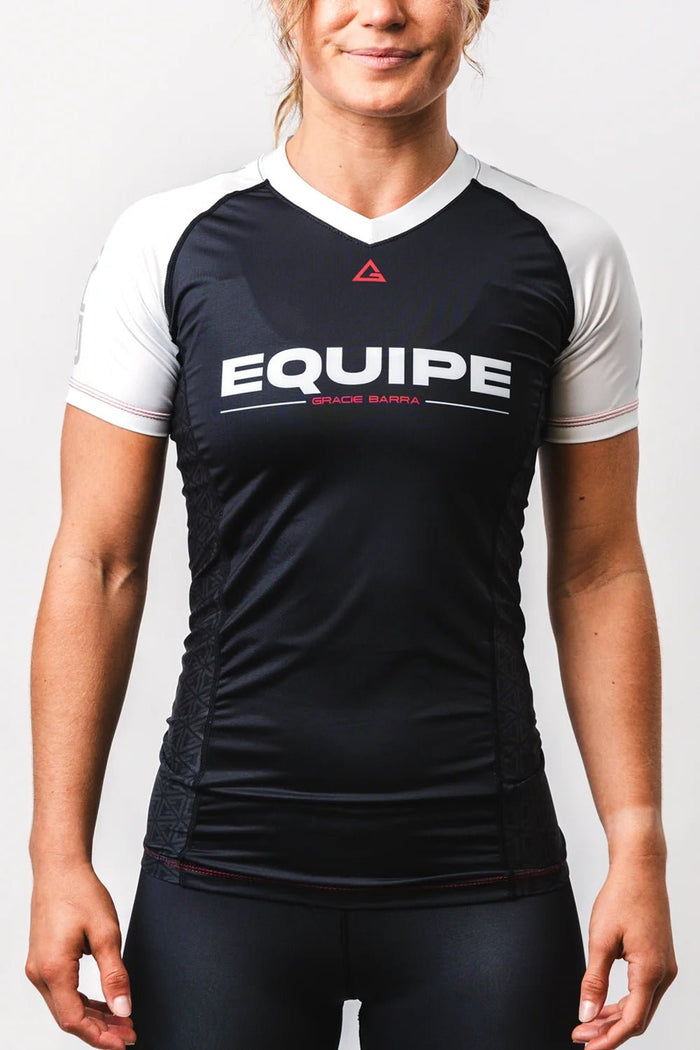 Woman wearing the GB Essentials Womens Ranked Rashguard in white, front view from the waist up showing the EQUIPE chest print and white raglan sleeves