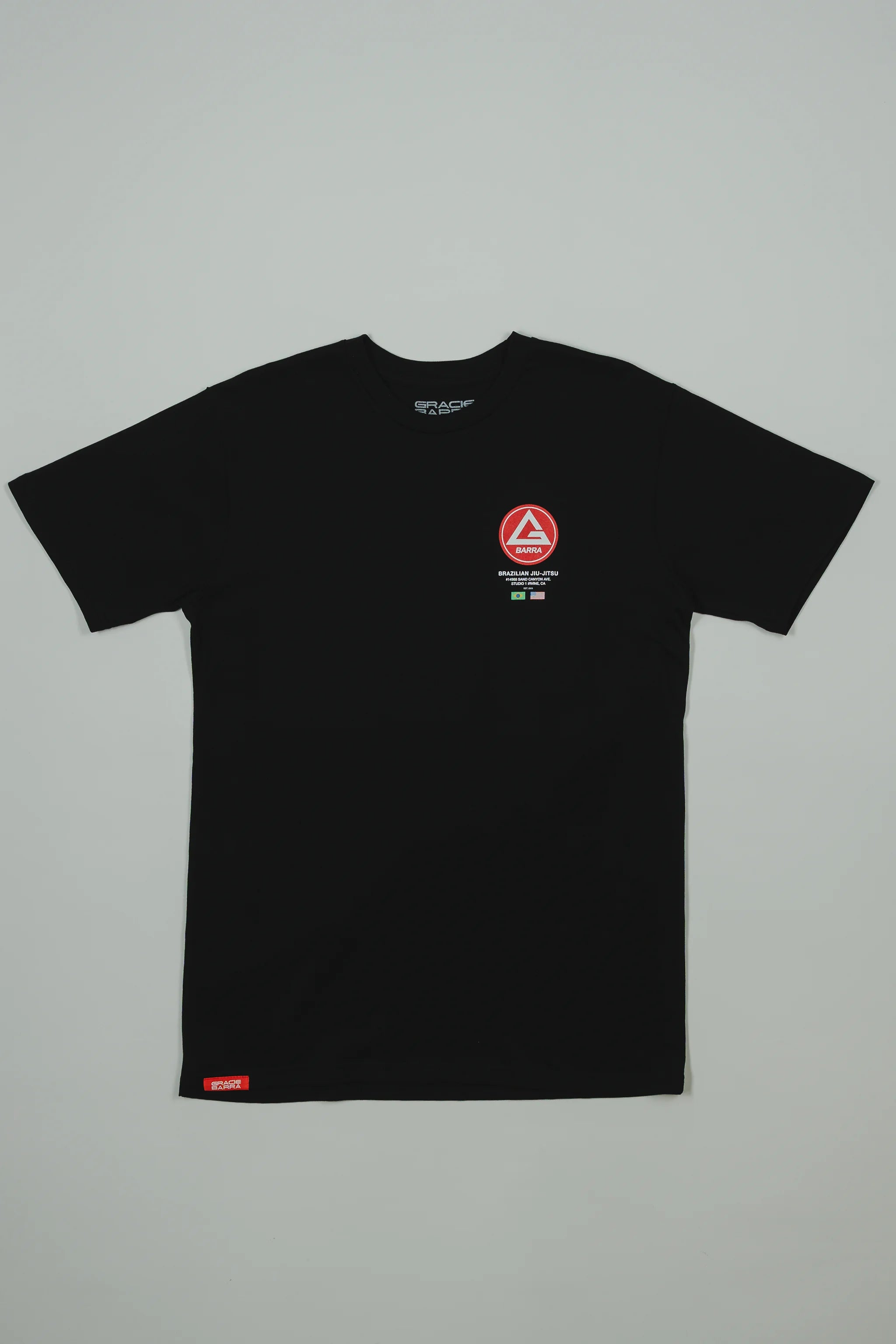Black GB HQ 20th Anniversary Tee laid flat on a light gray background, featuring the red Barra Shield on the left chest and woven GB Wear label at the hem.