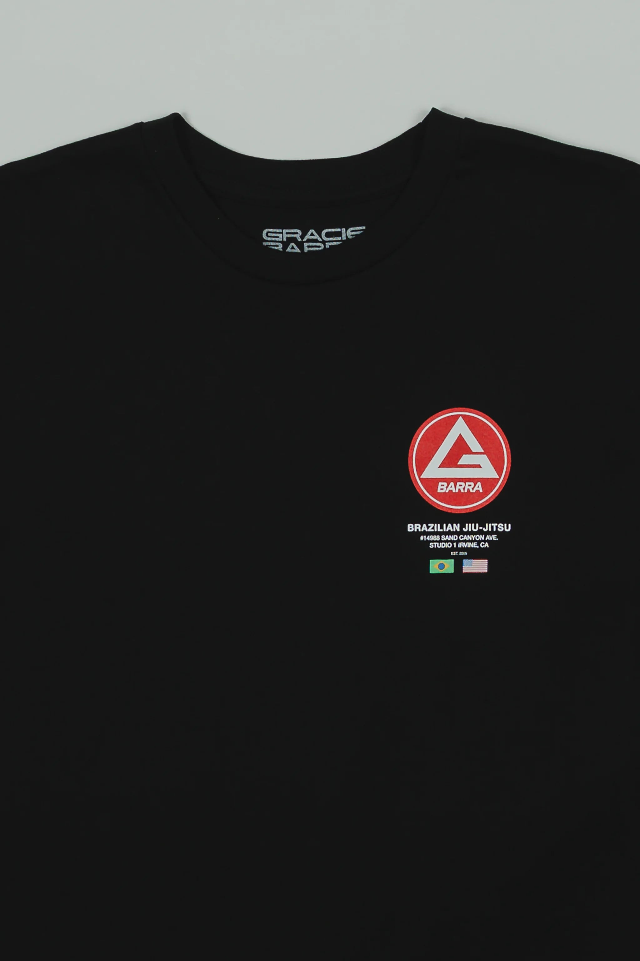 Close-up of the black GB HQ 20th Anniversary Tee showing the red Barra Shield chest emblem with ‘Brazilian Jiu-Jitsu’ text and the Brazil and USA flags beneath it.