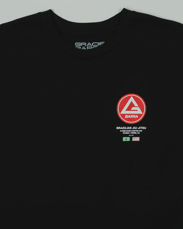 Close-up of the black GB HQ 20th Anniversary Tee showing the red Barra Shield chest emblem with ‘Brazilian Jiu-Jitsu’ text and the Brazil and USA flags beneath it.