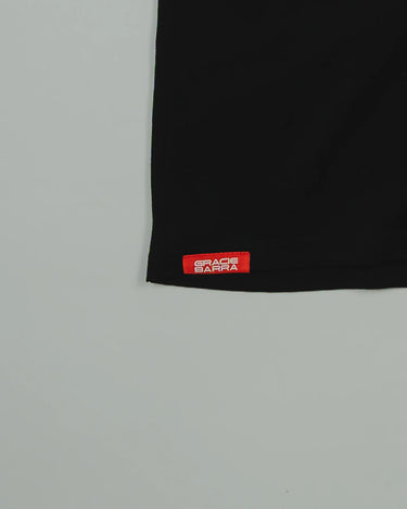 Close-up of the hem on the black GB HQ 20th Anniversary Tee, featuring the red woven Gracie Barra Wear label against a light gray background.