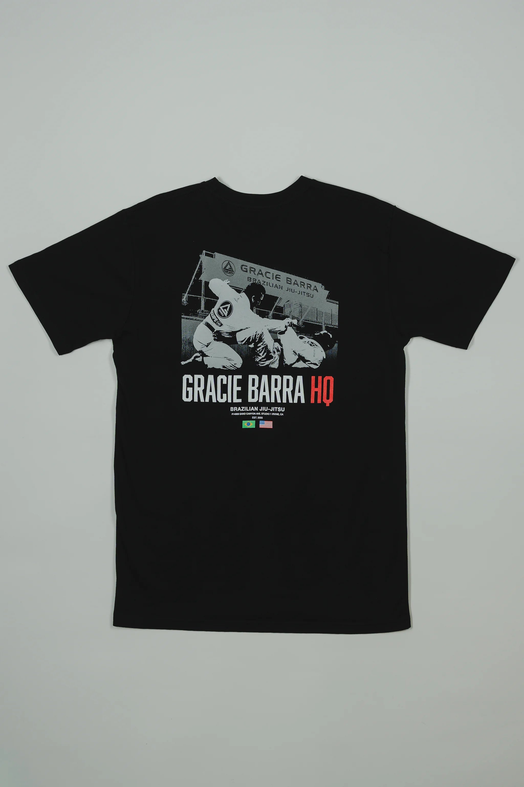 Back view of the black GB HQ 20th Anniversary Tee laid flat, featuring a grayscale photo of GB athletes sparring inside the original Irvine HQ with ‘Gracie Barra HQ’ text and Brazil and USA flags beneath.