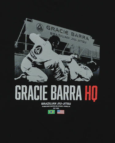 Close-up of the back graphic on the black GB HQ 20th Anniversary Tee, showing GB athletes sparring in front of the original Irvine Headquarters with ‘Gracie Barra HQ’ text and Brazil and USA flags.