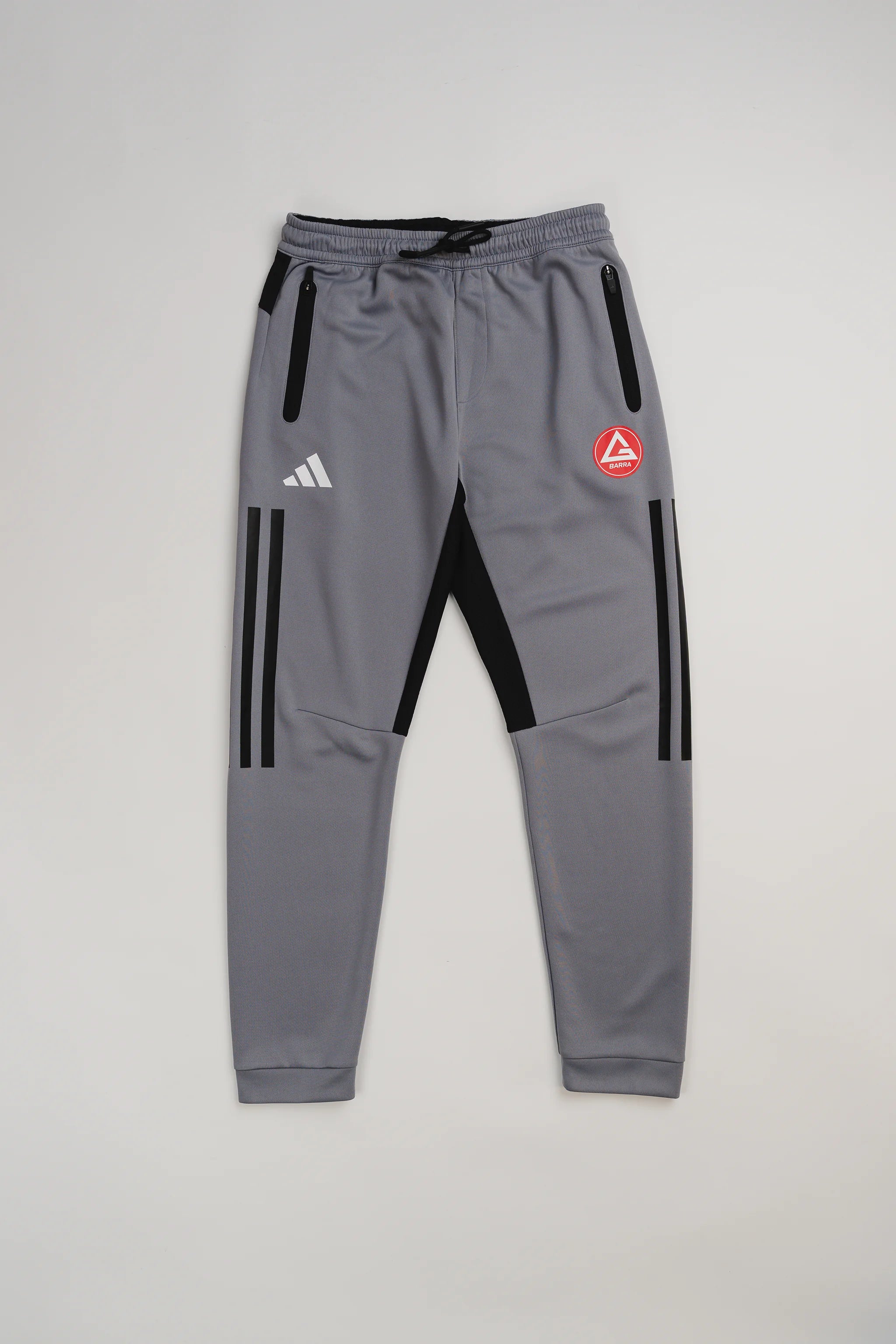 Gray GB Team Track Jogger by adidas with black stripes, red Gracie Barra logo, and drawstring waistband on a light gray background.