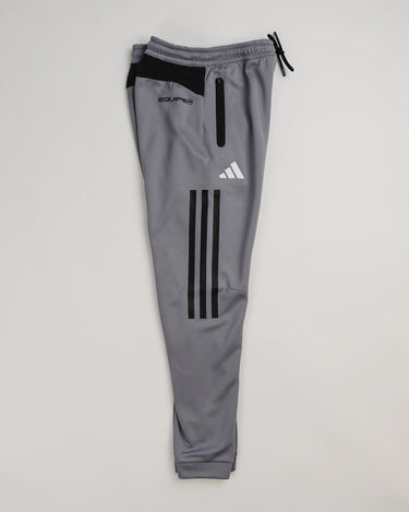 Gray GB Team Track Jogger by adidas folded with black stripes and adidas logo visible, light gray background.