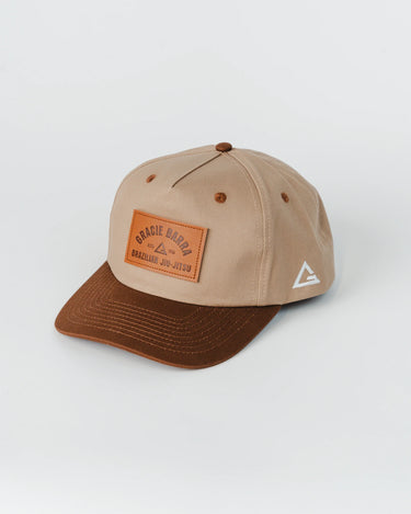 Beige and brown 5-panel GB Trademark Cap featuring a curved visor, embossed leather Gracie Barra patch on the front panel, and white logo embroidery on the left side, photographed flat against a white background.
