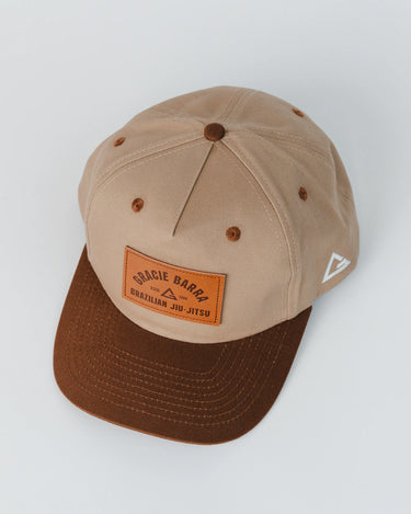 Beige and brown 5-panel cap with embossed Gracie Barra leather patch and mesh paneling, photographed from a high angle on a white background.