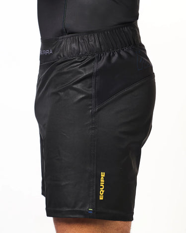 Side view of athlete wearing black Gracie Barra x Vanguard Evolution No Gi Shorts with yellow “Equipe” branding on leg and tonal stitching.