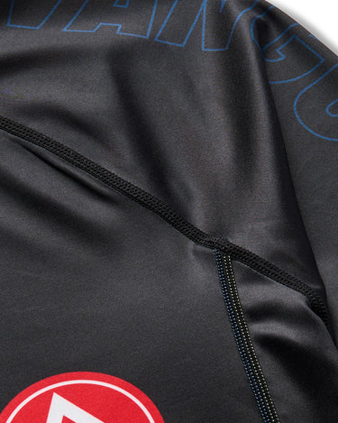 Detail view of black Gracie Barra x Vanguard Evolution rashguard showing reinforced flatlock stitching, tonal blue “Vanguard” branding, and partial red Barra Shield logo.