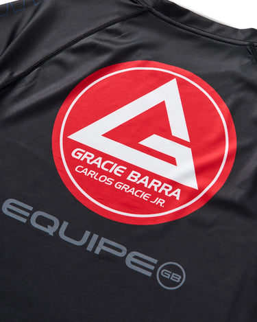 Close-up of black Gracie Barra x Vanguard Evolution rashguard back showing large red Barra Shield logo with “Gracie Barra Carlos Gracie Jr.” and grey “Equipe GB” lettering.