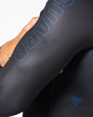 Close-up of black Gracie Barra x Vanguard Evolution rashguard sleeve with tonal blue “Vanguard” branding and triangle detail near elbow.