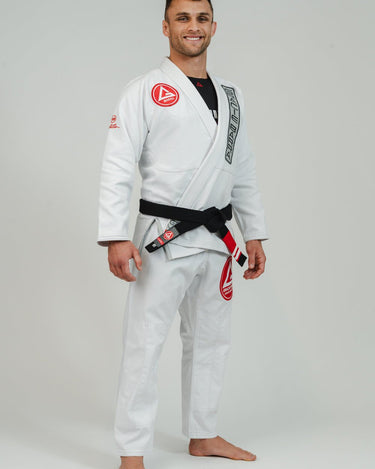 Adult athlete wearing the white GB1 Kimono in an angled front stance, showing the Red Shield chest patch, Gracie Barra lapel patch, reinforced jacket structure, and tapered performance fit.