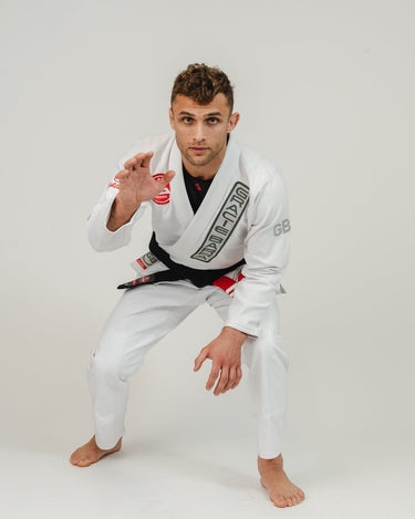Adult athlete wearing the white GB1 Kimono in a sparring stance, showing the Red Shield chest patch, Gracie Barra lapel patch, and reinforced design built for training intensity.