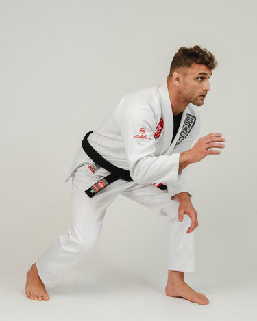 Adult athlete wearing the white GB1 Kimono moving forward in a training stance, highlighting the Red Shield chest patch, Gracie Barra branding, and durable, reinforced construction.