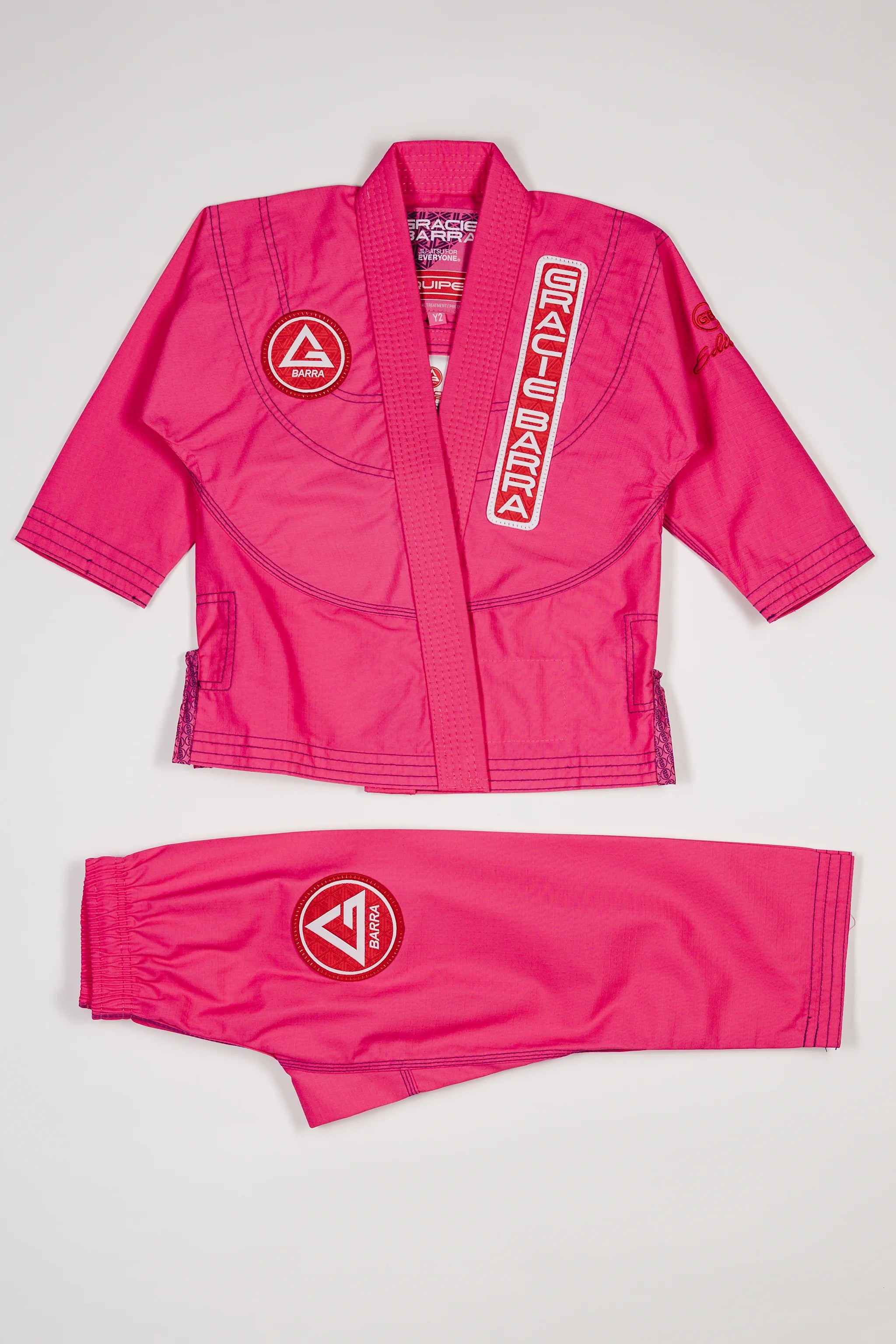 Pink GBK Lite Ripstop kids’ kimono set with Red Shield patches, a Gracie Barra lapel patch, and a GB label at the bottom of the lapel. Jacket and pants are shown clearly to help parents see the fit, color, and details perfect for young girls starting their Jiu-Jitsu journey.