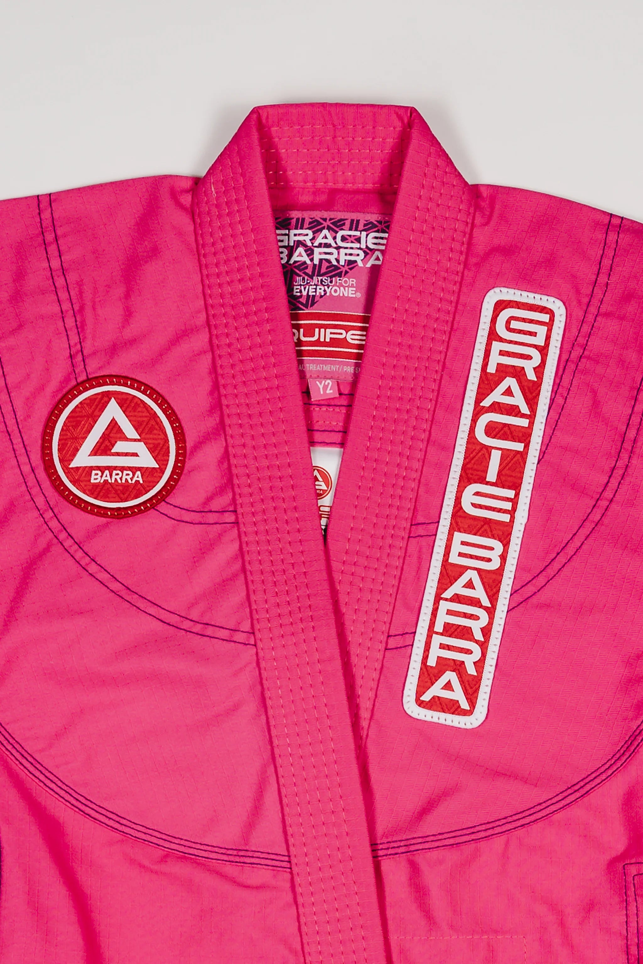 Close-up of the pink GBK Lite Ripstop kimono showing the Red Shield chest patch, the Gracie Barra lapel patch, and reinforced collar stitching—details parents appreciate for comfort and durability.