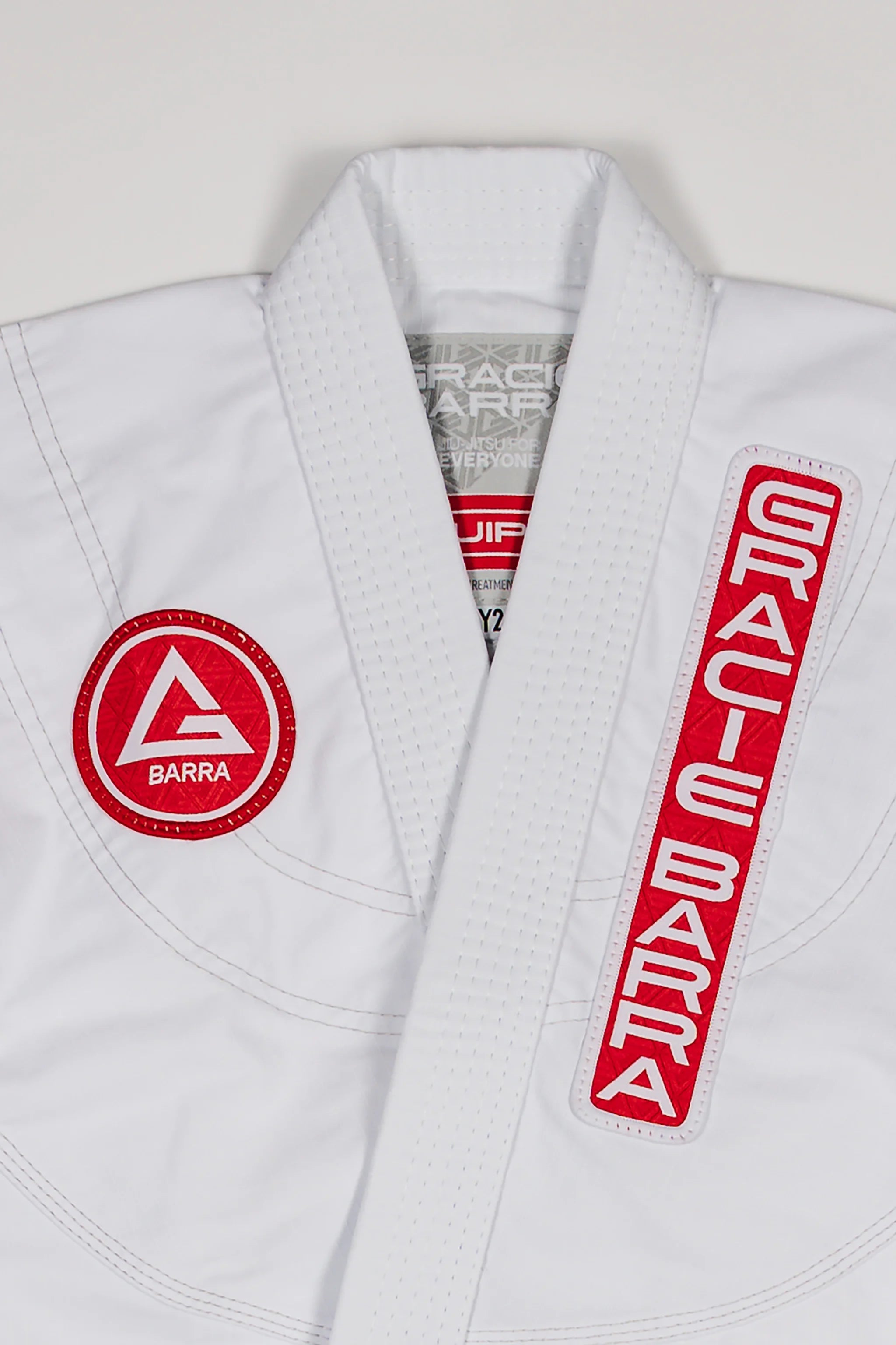 Close-up of Red Shield patch and Gracie Barra vertical patch on the white kids’ kimono.