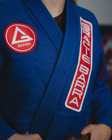 Close-up of blue GB x adidas III Stripes Women’s Kimono showing red Barra Shield patch on chest and red Gracie Barra lapel patch worn during training.