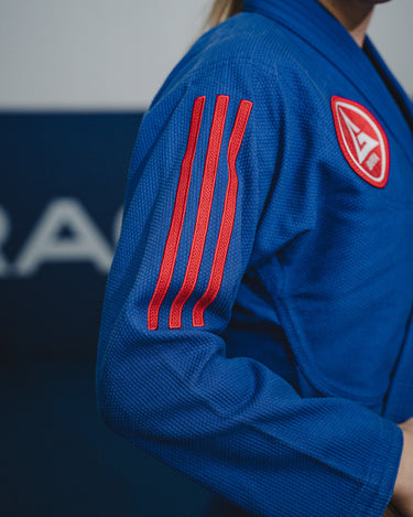 Close-up of blue GB x adidas III Stripes Women’s Kimono sleeve showing bold red 3-Stripes detail and Barra Shield patch during training at a Gracie Barra.