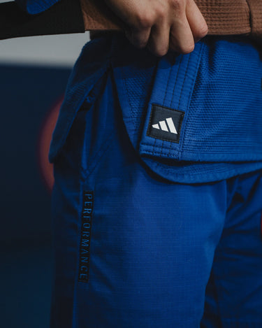 Close-up of blue GB x adidas III Stripes Women’s Kimono during training, showing embroidered adidas logo and Performance text above lightweight ripstop pants.