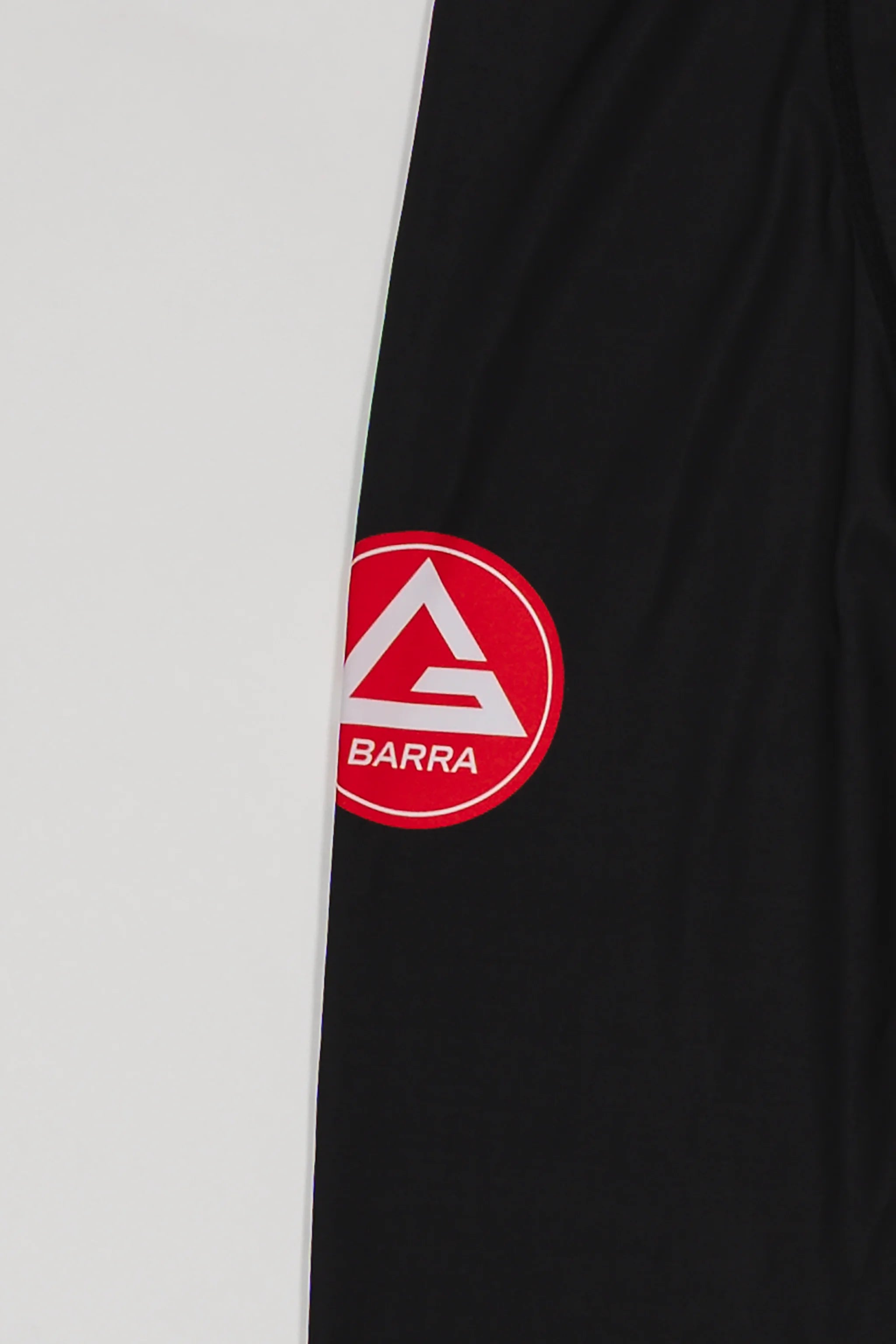 Close-up of the GB x adidas III Stripes Compression Pants showing the Red Shield logo printed on black performance fabric.