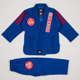 Close-up of blue GB x adidas III Stripes Youth Kimono jacket showing red Gracie Barra patch on lapel, GB Red Shield on chest, and adidas logo at collar on white background.