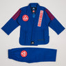 Close-up of blue GB x adidas III Stripes Youth Kimono jacket showing red Gracie Barra patch on lapel, GB Red Shield on chest, and adidas logo at collar on white background.