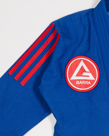 Close-up of blue GB x adidas III Stripes Youth Kimono shoulder showing bold red 3-Stripes detail and Gracie Barra Red Shield patch on white background.
