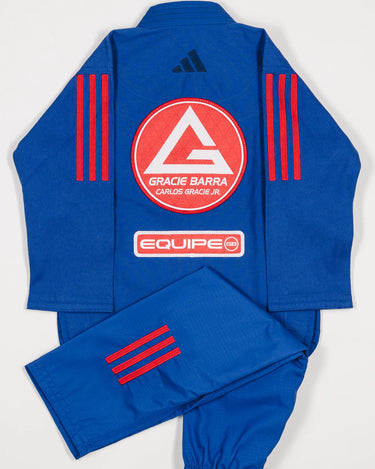 Back view of blue GB x adidas III Stripes Youth Kimono with pants folded across jacket, featuring large Red Shield patch, red 3-Stripes on shoulders and pant leg, and adidas logo at upper back.