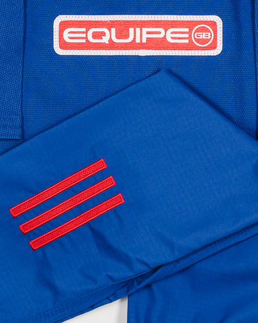 Close-up of blue GB x adidas III Stripes Youth Kimono pants and jacket showing red 3-Stripes detail on pant leg and red EQUIPE GB patch on jacket back.