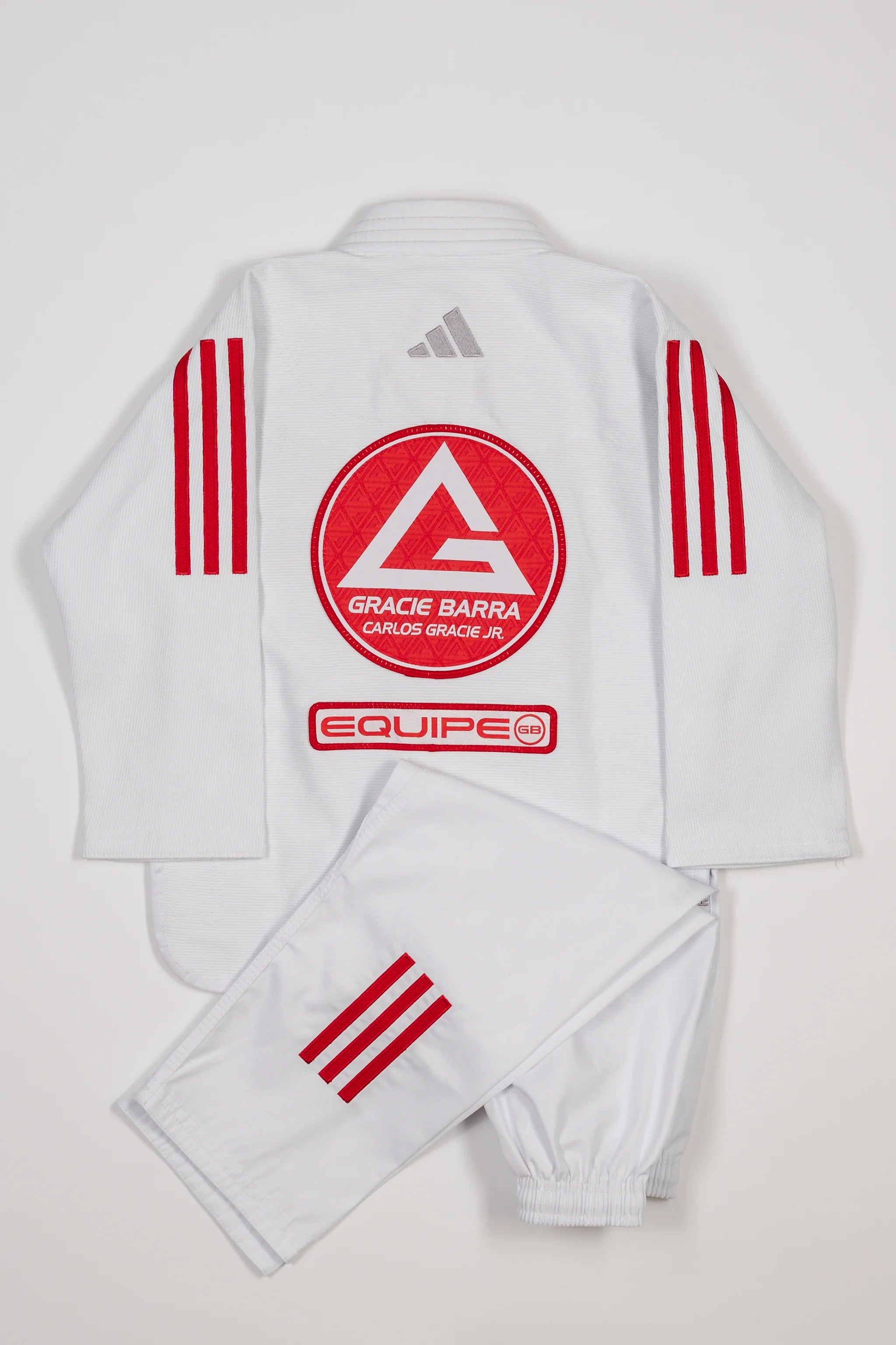 Back view of white GB x adidas III Stripes Youth Kimono with pants folded across jacket, featuring large Red Shield patch, red EQUIPE GB patch, and bold red 3-Stripes on shoulders and pant leg.